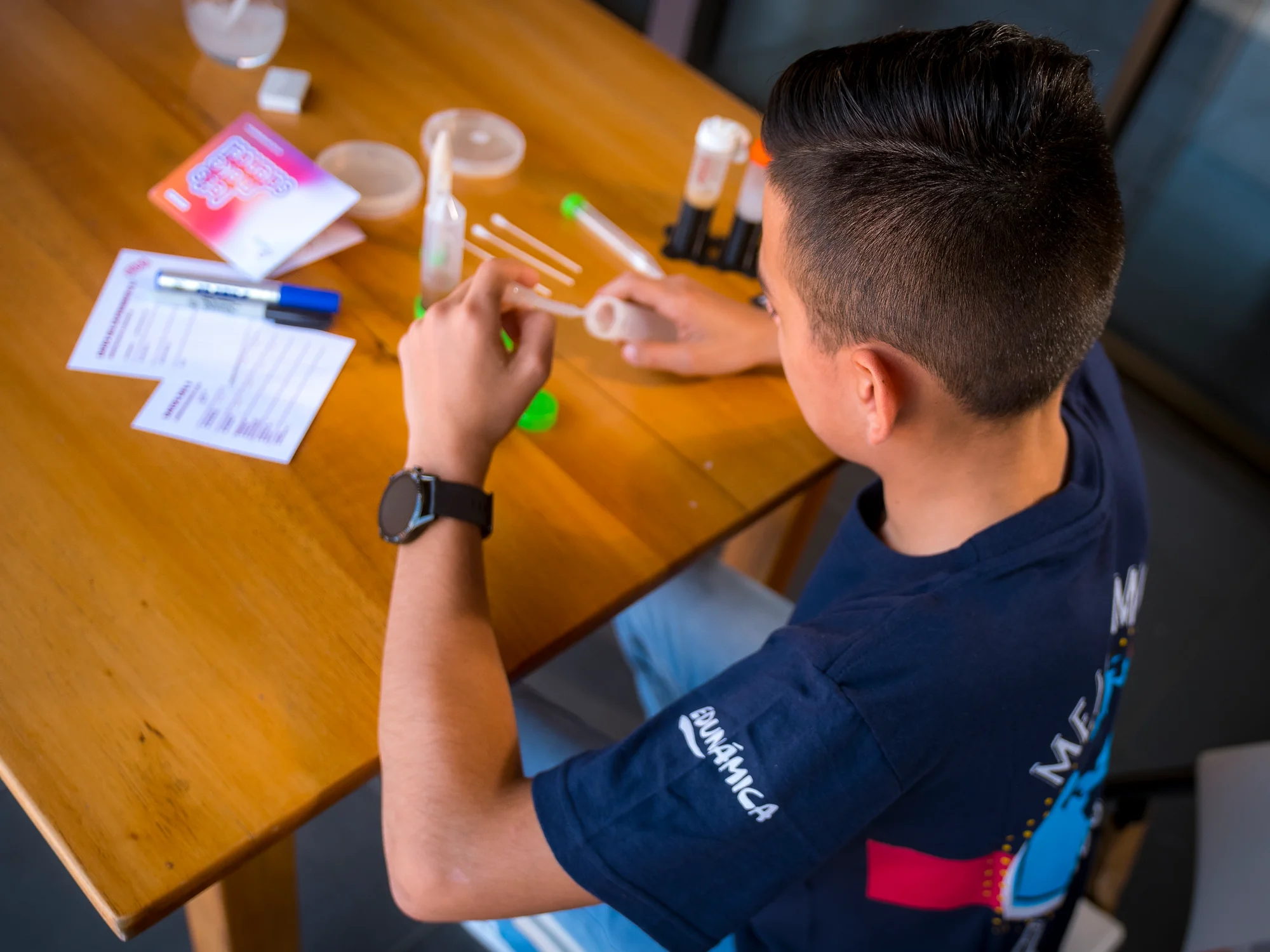 Edunámica beneficiary preparing his science experiment on a wooden table, overhead view
