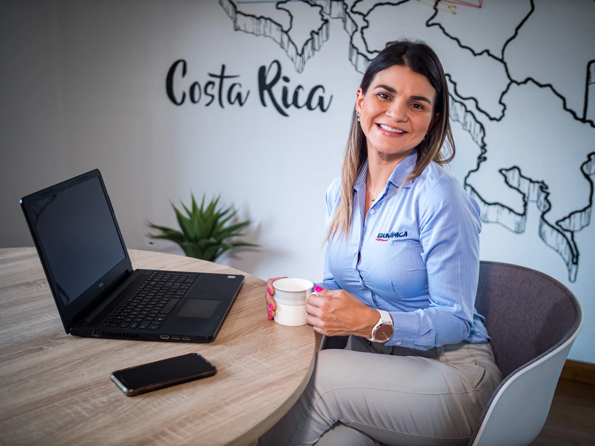 Institutional portrait of an Edunámica staff member holding a coffee mug, in front of a mural with a map of Costa Rica