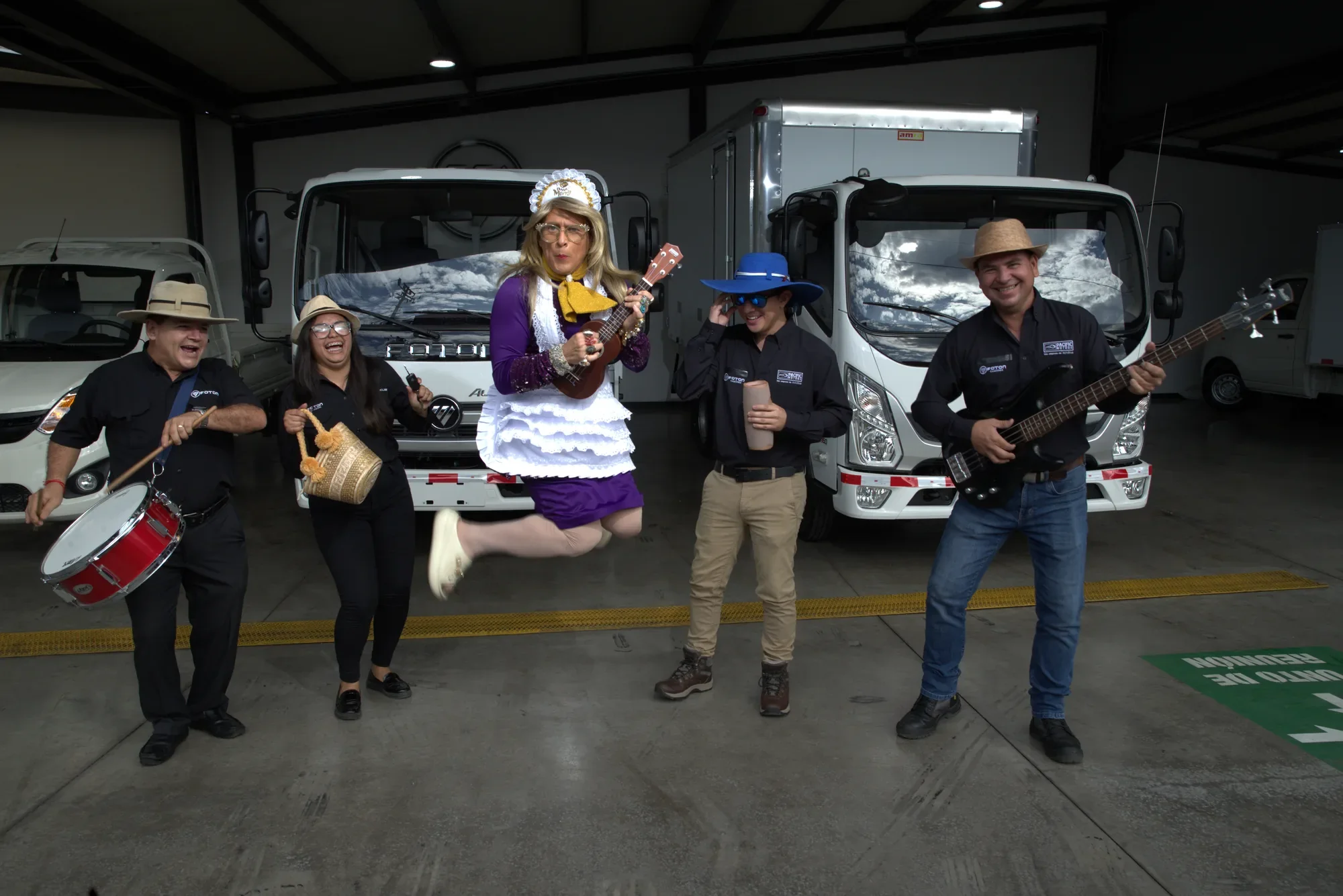 Doña Merry jumps with a ukulele alongside the Pacific Motors team in front of the Foton trucks