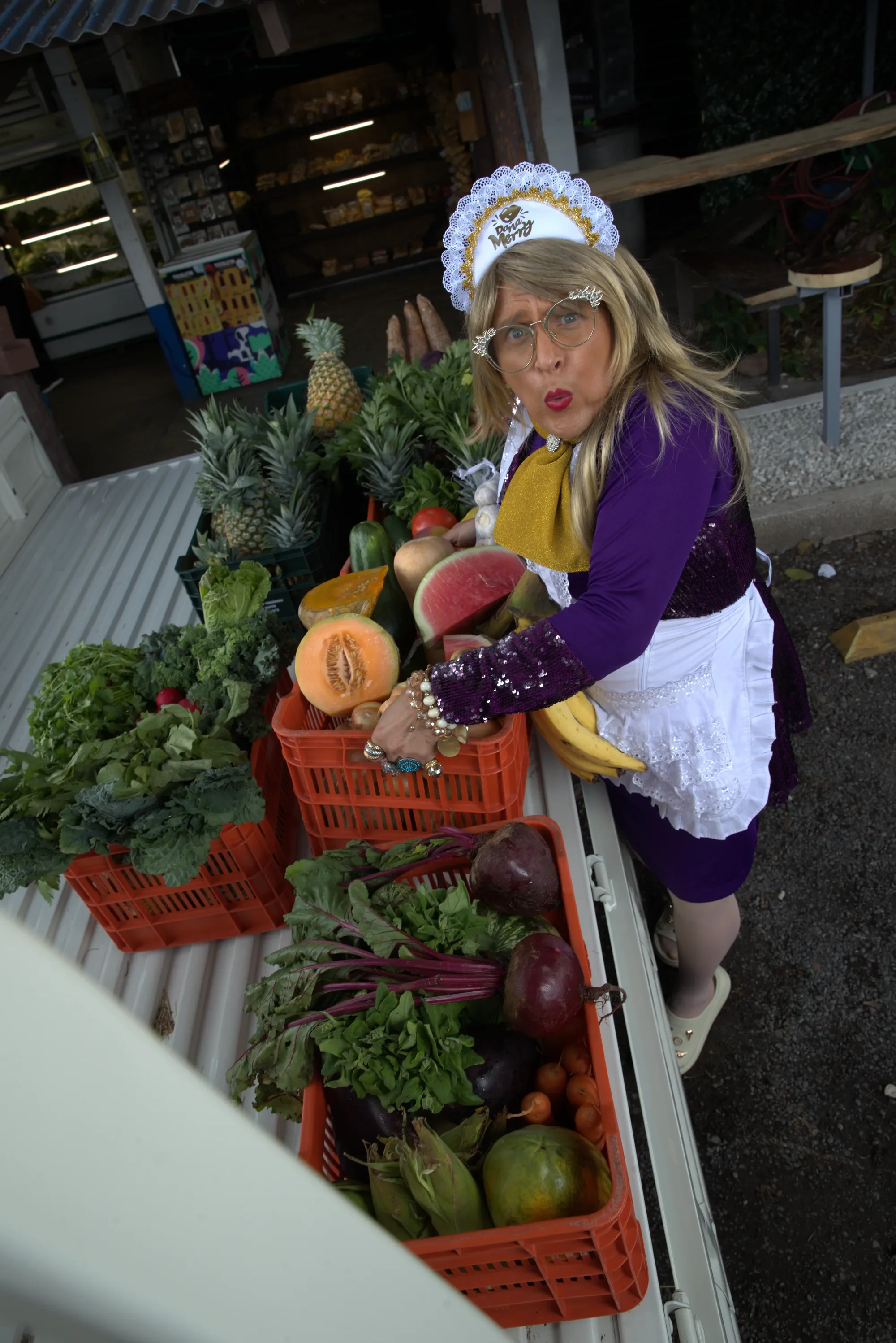 Doña Merry among crates of fruit and vegetables at a farmers' market